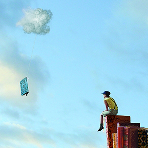 Visuel: un homme de dos est assis sur un livre debout, dans le ciel bleu, un livre tombe d’un nuage