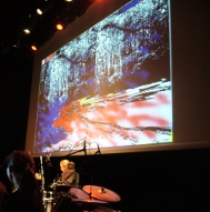 Scène de ¾ avec batterie au premier-plan et écran de projection