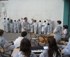 En combinaison de peintre, de dos, un orchestre d’élèves, au fond, des élèves peignent sur un mur