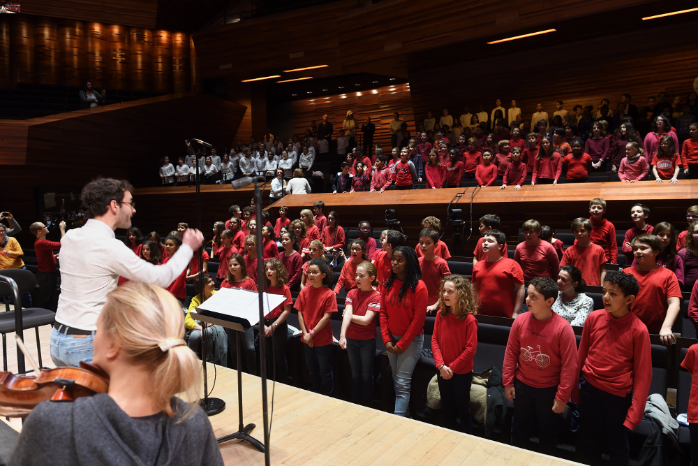 Le 25/1/2018 à l’Auditorium, les élèves chantent en rouge, à gauche de dos, Gaétan Biron dirige