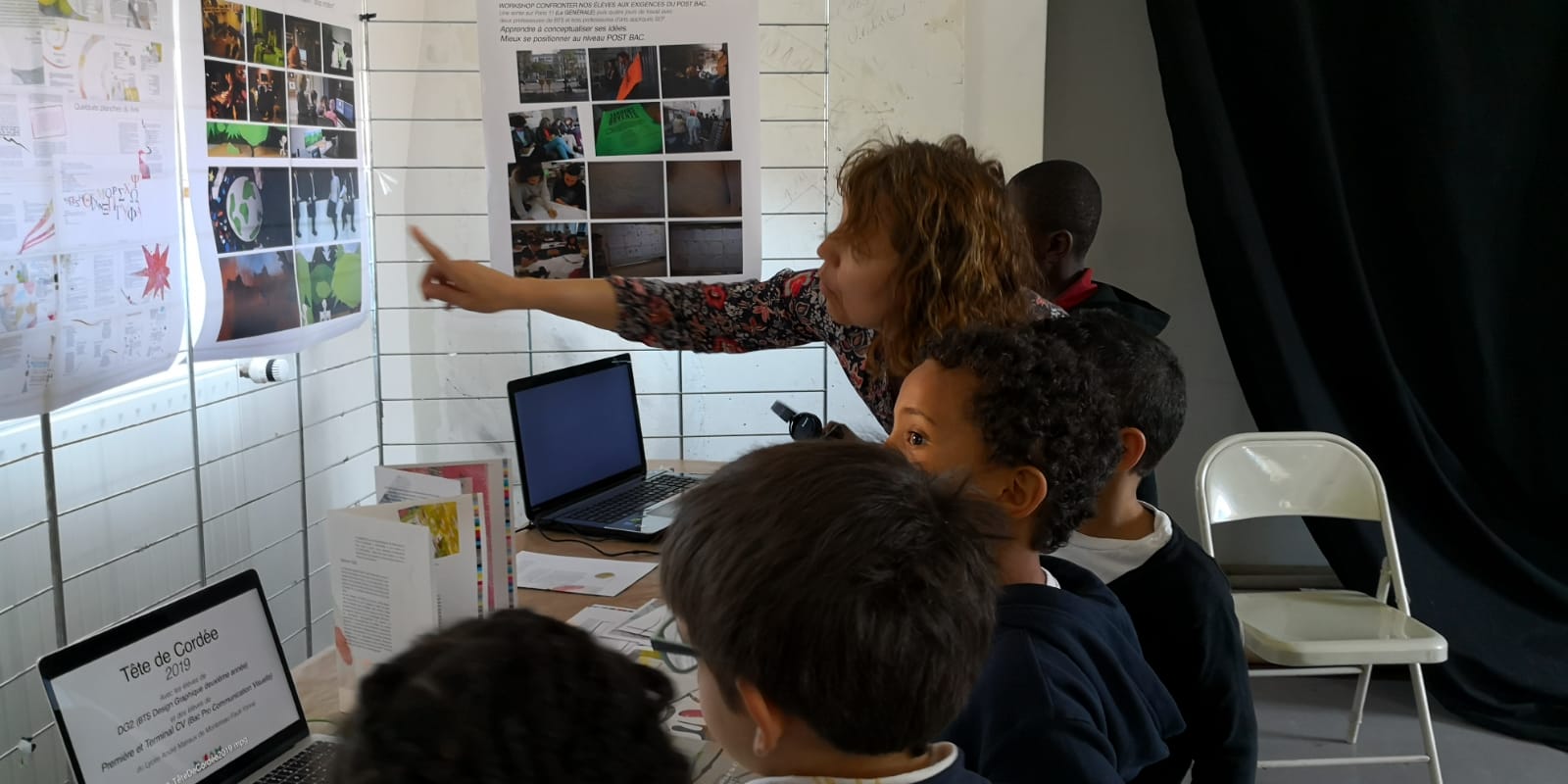 Une enseignante montre un panneau à 4 CP devant le portable, sur l’écran ‘Tête de Cordée 2019’