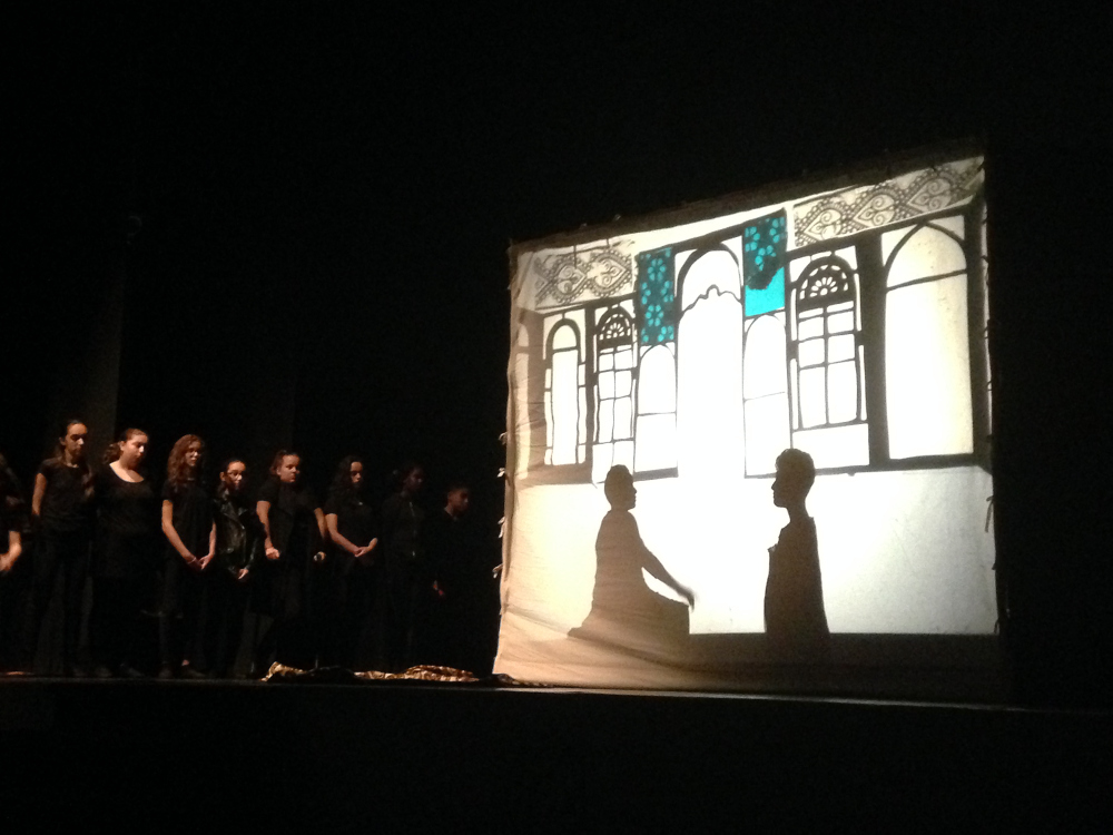 Sur scène, 6 élèves à côté d’un écran : en ombre, 2 personnes assises dans un palais