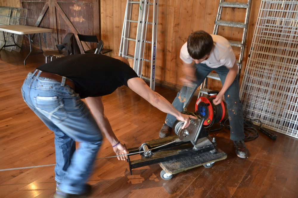 Un jeune et un adulte enroulent un câble d’acier autour d’un treuil dans un atelier
