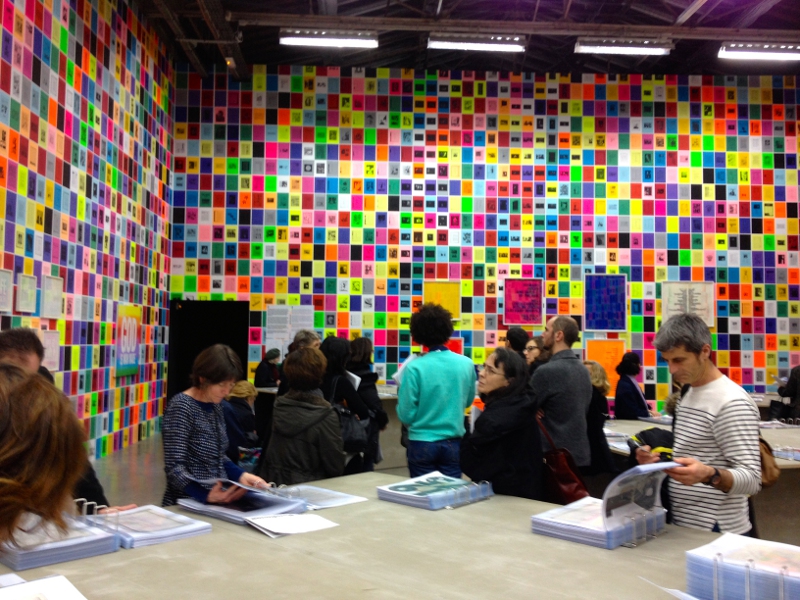 Les visiteurs compulsent des classeurs, les murs sont couverts de carreaux colorés et illustrés