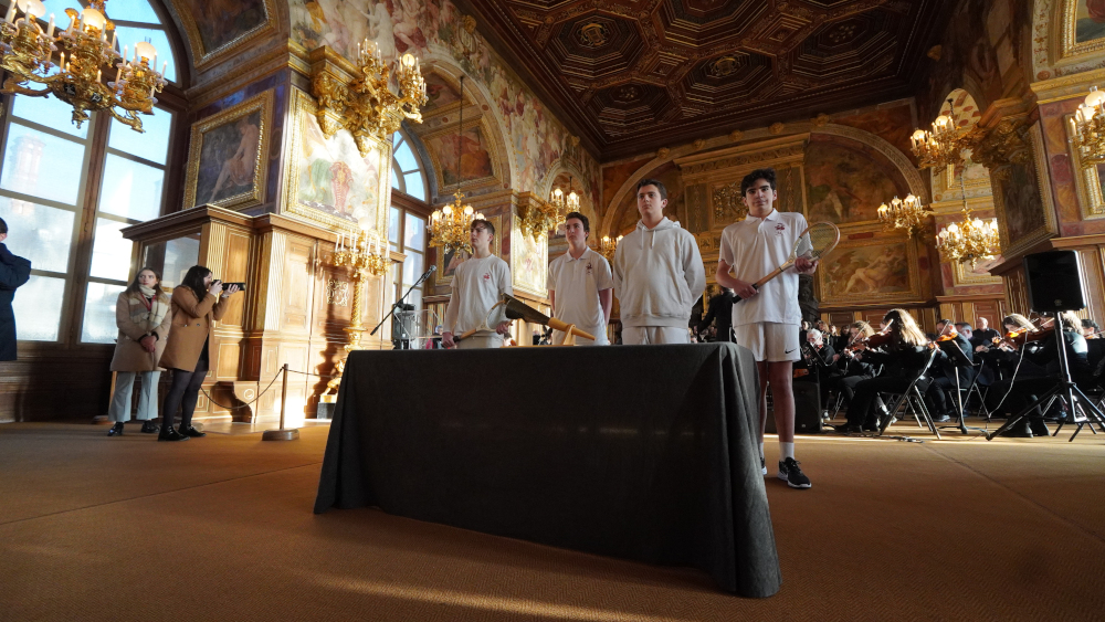 Dans la salle de bal du château de Fontainebleau, 4 joueurs de paume de l’UNSS devant le flambeau