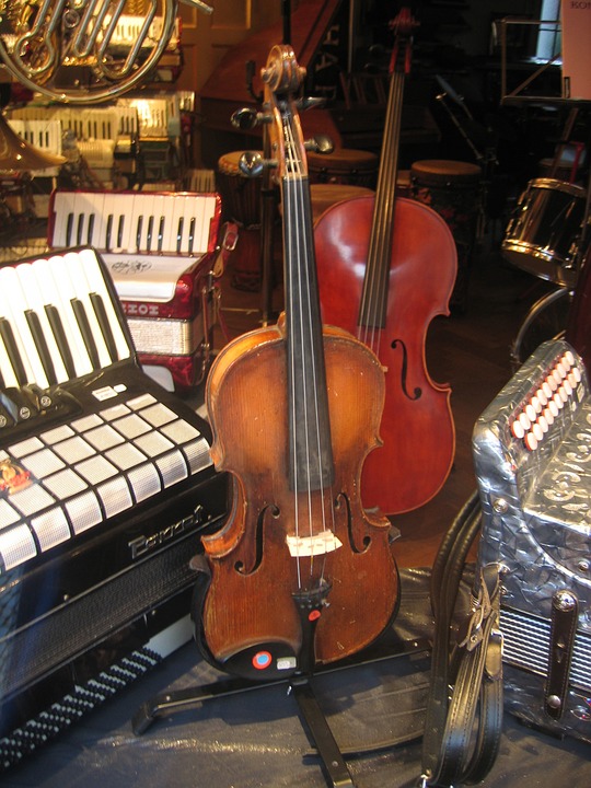 Un violon sur un socle devant un violoncelle, sur les côtés et derrière, des accordéons et un cor