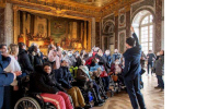 Un médiateur montre le plafond du salon d’Hercule du château de Versailles à des visiteurs PMR
